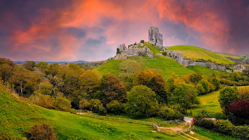 Corfe Castle from a distance with clouds lit by the setting sun in the sky