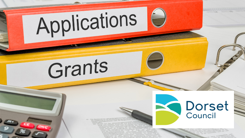 Desk with 2 binders labelled applications and grants with a notebook, calculator and pen. Dorset Council logo is in bottom right