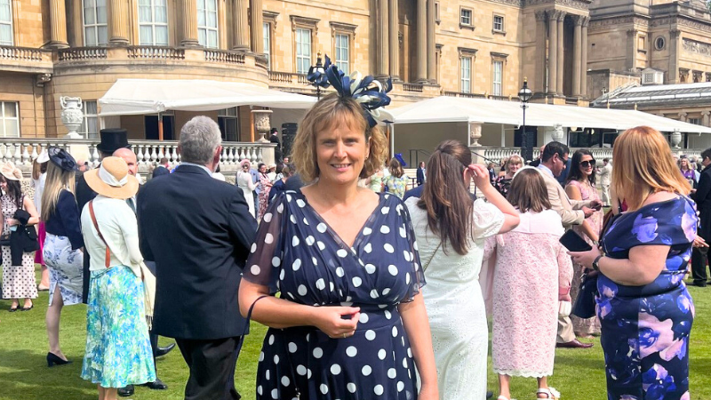 Catherine Horsley, town clerk at Corfe Mullen, int he garden of Buckingham Palace. Catherine is wearing a navy blue dress with large white polka dots and a navy blue fascinator on her head