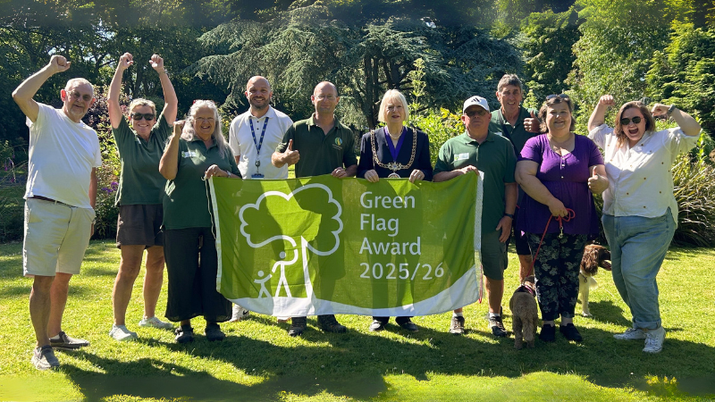 Group of people in a park cheering and holding a Green Flag Award banner