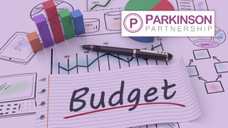 Piece of paper with Budget written on it in marker pen. Paper is on top of finance sketches with chart blocks and a pen